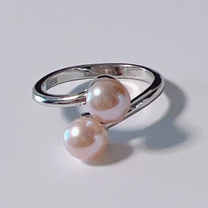 May include: A silver ring with two pink pearls. The ring is twisted and the pearls are set on either side of the twist.