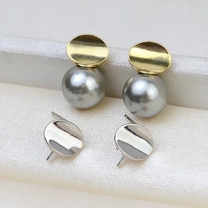 May include: A pair of silver and gold earrings with a pearl-like bead and a round disc. The earrings are on a white surface.