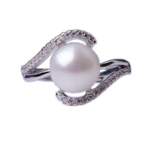 Puede incluir: Un anillo de plata con una gran perla blanca engastada en un diseño de espiral con pequeñas piedras transparentes.