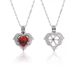 May include: A silver heart-shaped locket necklace with a red pearl inside. The locket is open to reveal a flower design inside. The necklace is on a silver chain.
