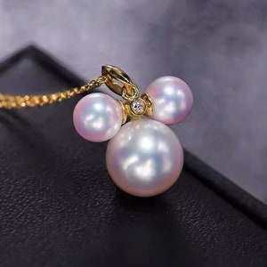 May include: A gold pendant necklace with three white pearls and a small diamond accent. The pearls are arranged in a cluster, with the largest pearl in the center.