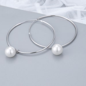 May include: A pair of silver hoop earrings with a white pearl dangling from each hoop.