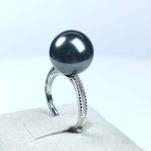 May include: A silver ring with a large, black pearl set on top. The ring has a delicate, beaded design on the band.