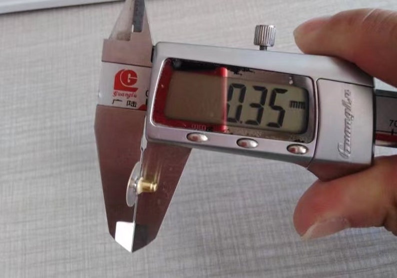 Puede incluir: Un calibre digital plateado que mide un peque&ntilde;o objeto de color dorado. El calibre muestra 0,35 mm.