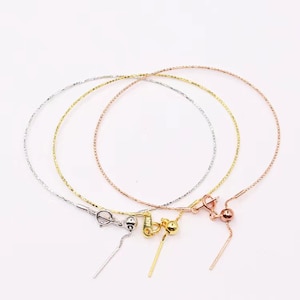 May include: Three delicate gold chains with different colored clasps. The chains are layered on top of each other and have a small ball at the end of each chain.