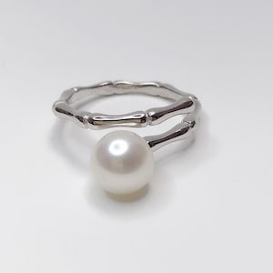 May include: A silver ring with a pearl set on a twisted band. The band is designed to resemble bamboo.