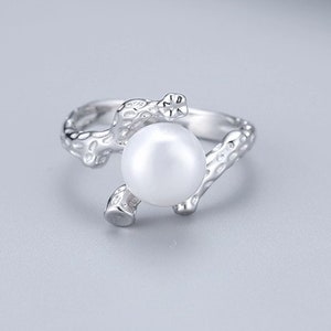 May include: A silver ring with a pearl set in a branch-like design.