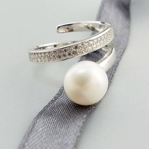 May include: A silver ring with a single pearl and a band of sparkling stones.