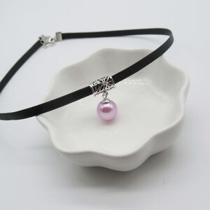 May include: A black choker necklace with a silver filigree charm and a single pink pearl pendant.