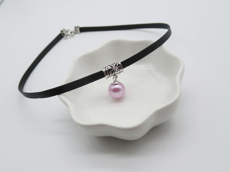 May include: A black choker necklace with a silver filigree charm and a single pink pearl pendant.