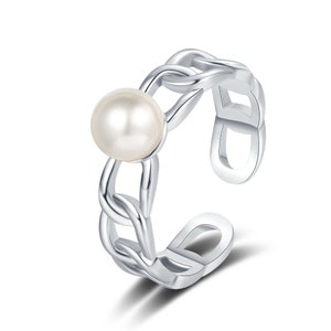 May include: A silver ring with a delicate chain design and a single white pearl in the center.