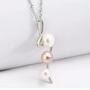 Puede incluir: Un collar de plata con un delicado colgante curvo con tres perlas. Las perlas son blancas y rosadas.