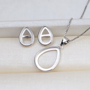 Könnte beinhalten: Eine silberne Halskette mit Anhänger und passende Ohrringe mit einer tropfenförmigen Fassung. Die Fassungen sind leer und bereit, mit einem Edelstein gefüllt zu werden.