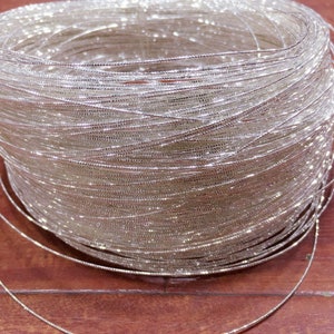 May include: A spool of silver metallic thread. The thread is wound tightly around the spool, creating a shimmering effect.