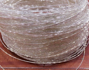 Puede incluir: Una bobina de hilo metálico plateado. El hilo está enrollado firmemente alrededor de la bobina, creando un efecto brillante.