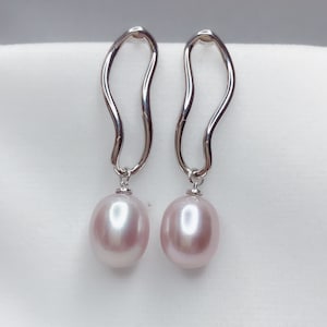 May include: A pair of silver earrings with a wavy design and a pink pearl dangling from each earring.