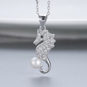 May include: A silver necklace with a seahorse pendant adorned with clear cubic zirconia stones and a single white pearl. The seahorse has a black eye.
