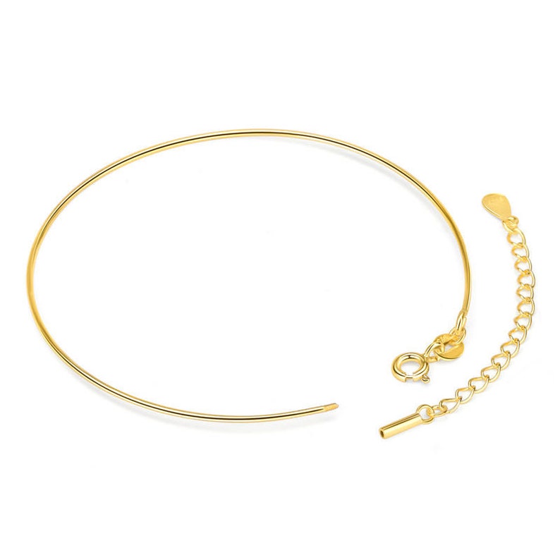 May include: A gold-colored necklace with a delicate, circular design. The necklace features a clasp and an adjustable chain for a customizable fit. The jewelry is displayed against a white background.