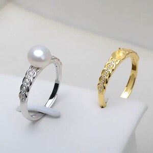 Puede incluir: Se muestran dos anillos. Uno es plateado con una perla blanca y pequeñas piedras transparentes. El otro es dorado con pequeñas piedras transparentes. Ambos anillos tienen un diseño de banda decorativa.