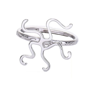 Könnte beinhalten: Silberring mit einem Kraken-Design. Der Kraken besteht aus dünnem Draht und hat acht Tentakel. Der Ringband ist ebenfalls aus Silber und hat ein zartes, graviertes Design.