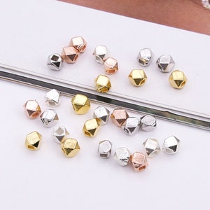Könnte beinhalten: Eine Sammlung geometrischer Perlen in Gold, Silber und Roségold. Die Perlen sind in Form eines fünfseitigen Würfels geformt und haben ein Loch in der Mitte zum Aufziehen.
