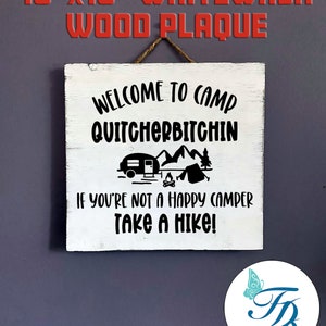 May include: A 10 inch by 10 inch whitewashed wooden plaque with black text that reads "Welcome to Camp Quitchherbitchin" and "If you're not a happy camper take a hike!"  The plaque features a black silhouette of a camper trailer, mountains, a campfire, and a tent.