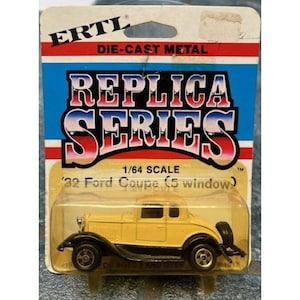 May include: A yellow die-cast metal '32 Ford Coupe (5 window) replica car. The car is a 1/64 scale model with black tires and trim. The packaging includes the text "REPLICA SERIES" and "DIE-CAST METAL".