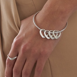 May include: A silver bangle bracelet with four heart-shaped charms. The charms are engraved with text.