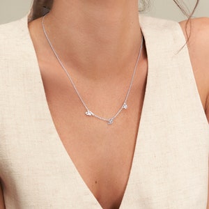May include: A delicate silver necklace featuring three cursive letter pendants. The necklace is displayed against a neutral background, highlighting the fine chain and the elegant design of the personalized jewelry.