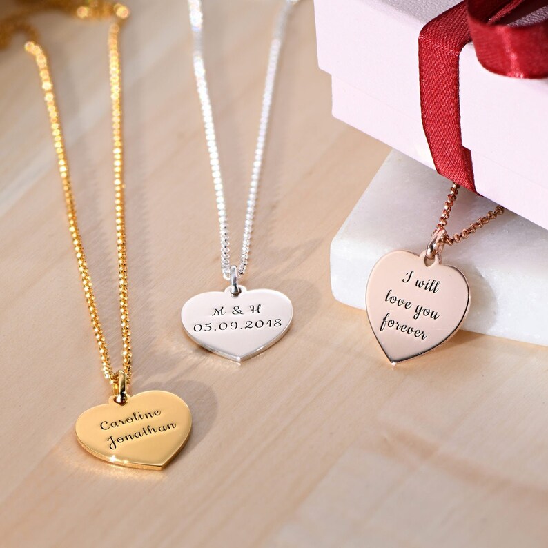 May include: Three gold, silver, and rose gold necklaces with heart-shaped pendants. The gold pendant is engraved with the text "Caroline Jonathan". The silver pendant is engraved with the text "M & H 05.09.2018". The rose gold pendant is engraved with the text "I will love you forever".