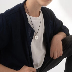 May include: A silver compass pendant necklace with a black cord. The pendant is shaped like a shield with a compass rose and the letters N and S.