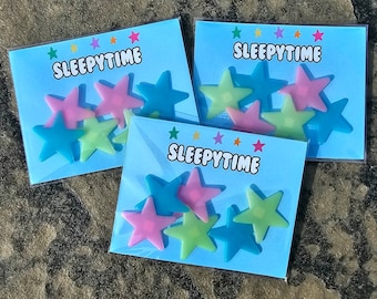 May include: Three packages of glow-in-the-dark star stickers. Each package has a blue background with the text "SLEEPYTIME" and features a variety of pink, blue, and green stars.