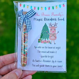 May include: A clear plastic tube filled with colorful sprinkles and a white and black checkered ribbon tied around the top. A white card with the text "The Bruce Family's Magic Reindeer Food" and instructions for using the sprinkles is behind the tube. The card also features a cartoon reindeer.