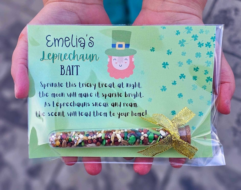 May include: A green card with the text "Emelia's Leprechaun Bait" and a cartoon leprechaun. The card is in a clear plastic bag with a small glass tube filled with colorful sprinkles tied with a gold ribbon.