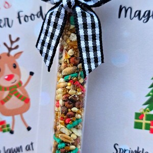 May include: A small glass tube filled with a mixture of colorful sprinkles, grains, and seeds. The tube is tied with a black and white checkered ribbon. The text on the card reads "Sprinkle the magic".