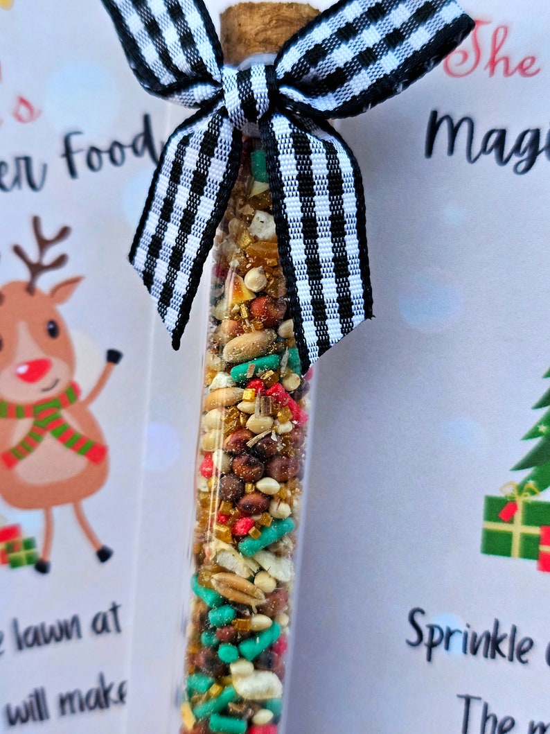 May include: A small glass tube filled with a mixture of colorful sprinkles, grains, and seeds. The tube is tied with a black and white checkered ribbon. The text on the card reads "Sprinkle the magic".