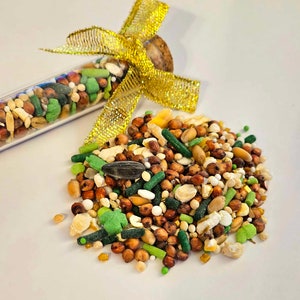 May include: A glass test tube filled with a variety of bird seed, tied with a gold ribbon. The tube is spilling out the seed onto a white surface.