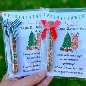 May include: Two clear plastic bags with white cards inside. Each card has a festive reindeer illustration and a poem about magic reindeer food. The bags contain small glass tubes filled with colorful sprinkles. The text on the cards reads "The Bruce Fam Magic Reindeer" and "Emelia's Magic Reindeer Food".