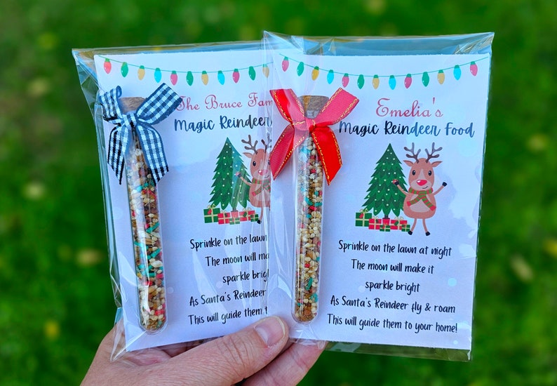 May include: Two clear plastic bags with white cards inside. Each card has a festive reindeer illustration and a poem about magic reindeer food. The bags contain small glass tubes filled with colorful sprinkles. The text on the cards reads "The Bruce Fam Magic Reindeer" and "Emelia's Magic Reindeer Food".
