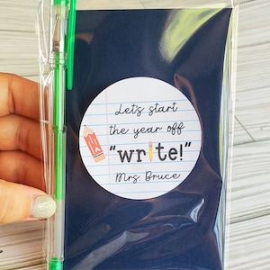 Puede incluir: Una tarjeta azul con un c&iacute;rculo blanco en ella. El c&iacute;rculo tiene un dibujo a l&aacute;piz y el texto "Let's start the year off "write!" Mrs. Bruce". Un bol&iacute;grafo verde est&aacute; al lado de la tarjeta.