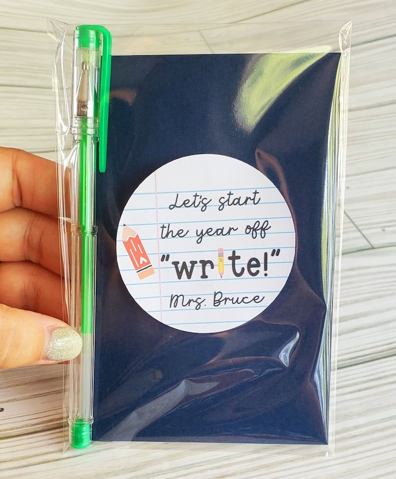 Puede incluir: Una tarjeta azul con un c&iacute;rculo blanco en ella. El c&iacute;rculo tiene un dibujo a l&aacute;piz y el texto "Let's start the year off "write!" Mrs. Bruce". Un bol&iacute;grafo verde est&aacute; al lado de la tarjeta.
