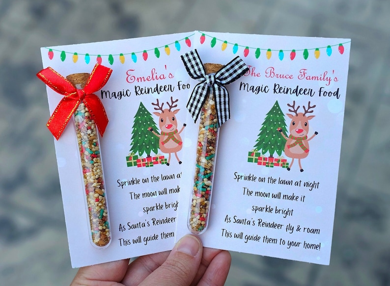 May include: Two small glass tubes filled with colorful sprinkles, tied with red and black ribbon, and attached to white cards with a reindeer illustration and instructions for "Magic Reindeer Food". The cards read "Emelia's Magic Reindeer Food" and "The Bruce Family's Magic Reindeer Food".