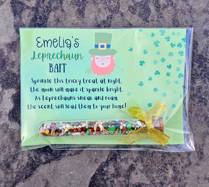 May include: A green card with the text "Emelia's Leprechaun Bait" and a cartoon leprechaun. The card is in a clear plastic bag with a gold ribbon and a small glass tube filled with colorful sprinkles.