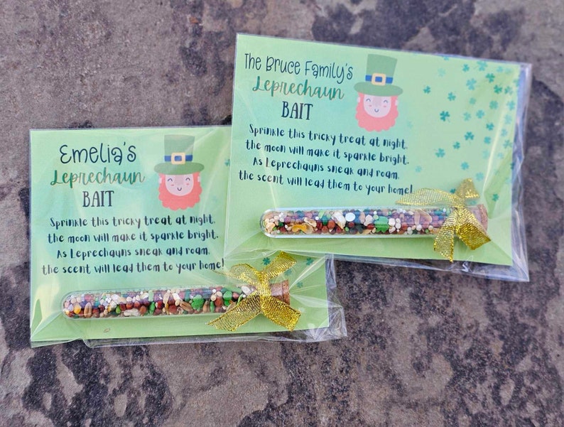 May include: Two green and white cards with instructions for a leprechaun bait. The cards have a picture of a leprechaun on them. The cards are in clear plastic bags with a small glass tube filled with colorful sprinkles. The tube is tied with a gold ribbon.