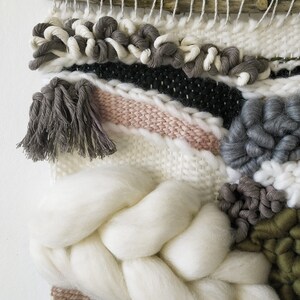 Detail of a woven wall hanging with an earthy, natural aesthetic. The wall hanging features a combination of olive green and beige tones, with textured, intricate weaving patterns.