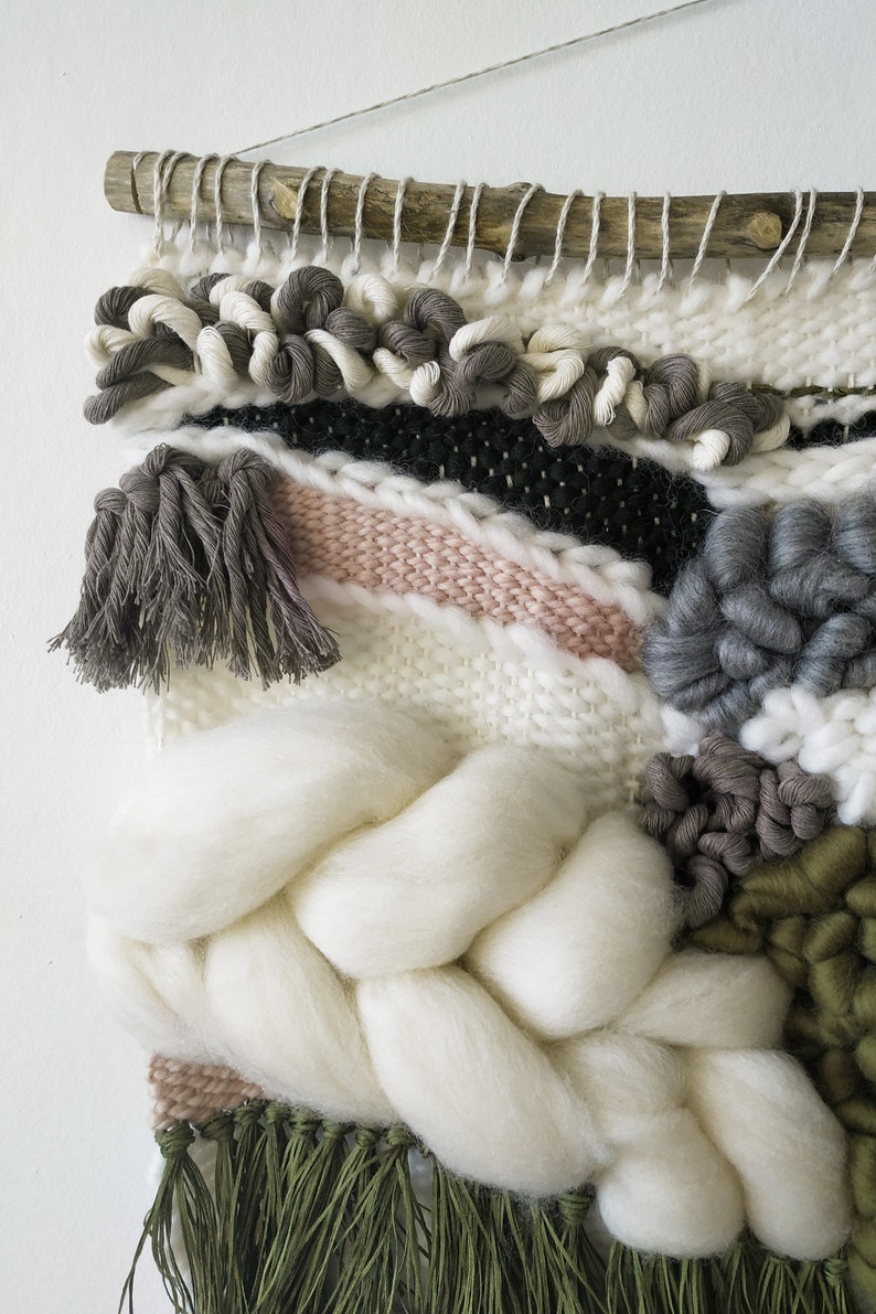 Detail of a woven wall hanging with an earthy, natural aesthetic. The wall hanging features a combination of olive green and beige tones, with textured, intricate weaving patterns.
