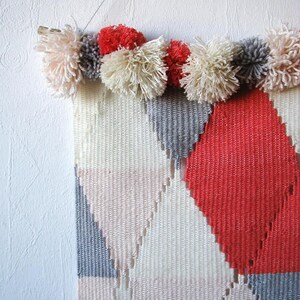 Detail of a woven wall hanging i pink, blue and beige