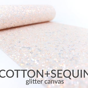 May include: A roll of white cotton fabric with a glittery, sequin-like texture. The fabric is labeled "COTTON+SEQUIN glitter canvas".