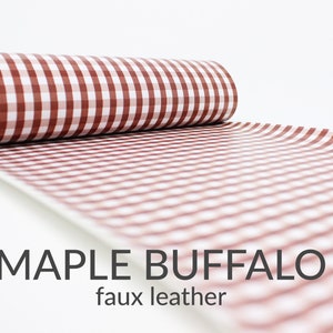 May include: A roll of red and white buffalo check faux leather fabric. The fabric has a checkered pattern and is rolled up on a white background.