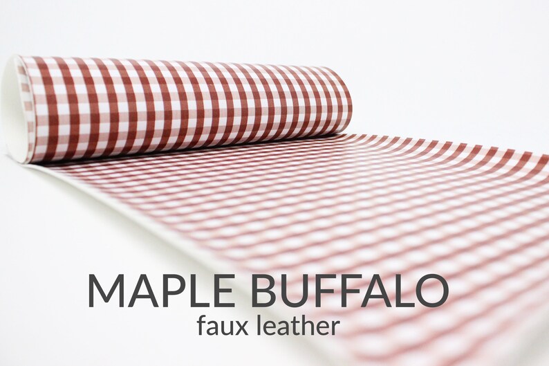 May include: A roll of red and white buffalo check faux leather fabric. The fabric has a checkered pattern and is rolled up on a white background.